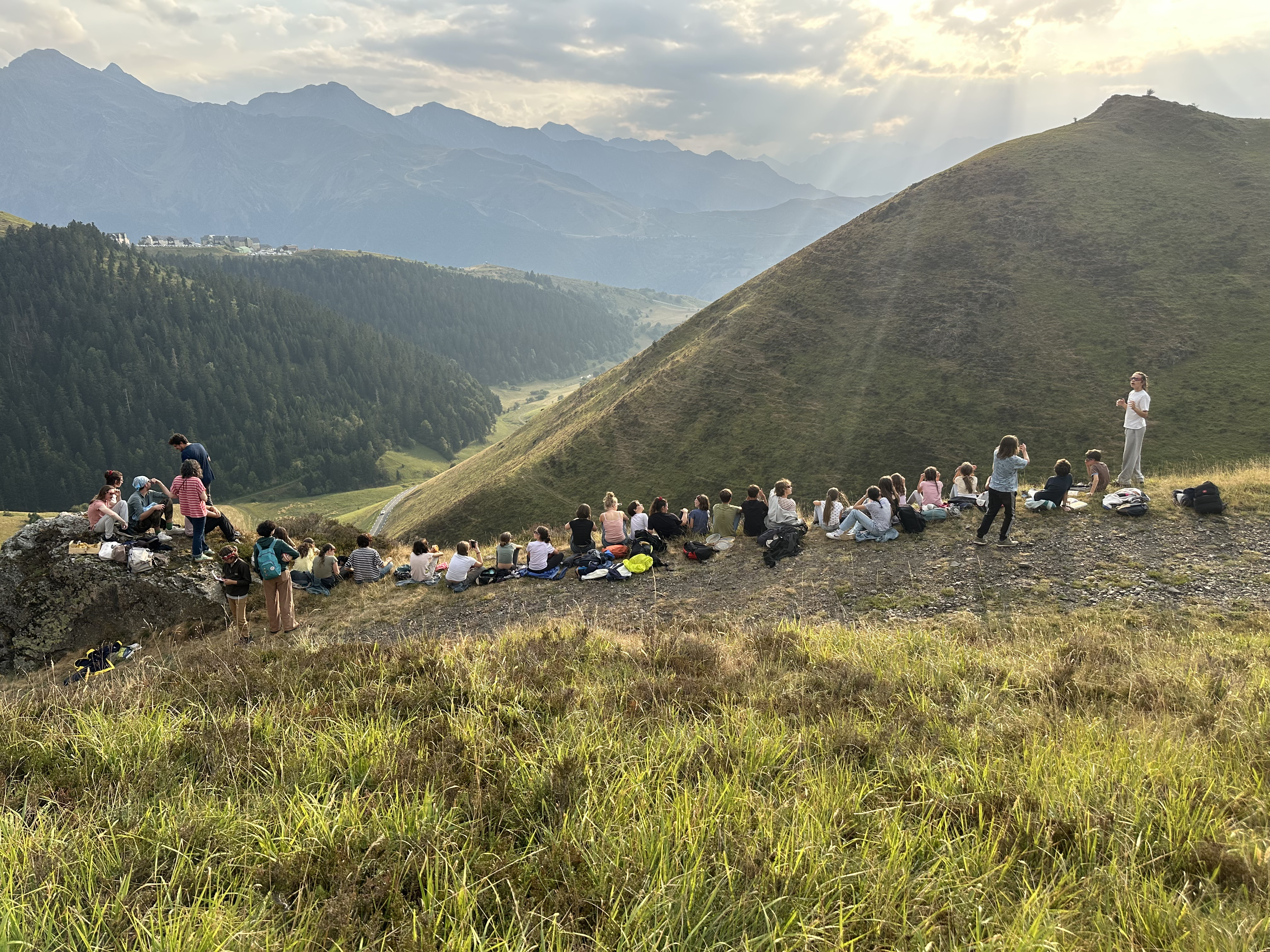 Groupe de jeunes assis en ligne sur une crête des Pyrénées au coucher du soleil, pendant un séjour EMS